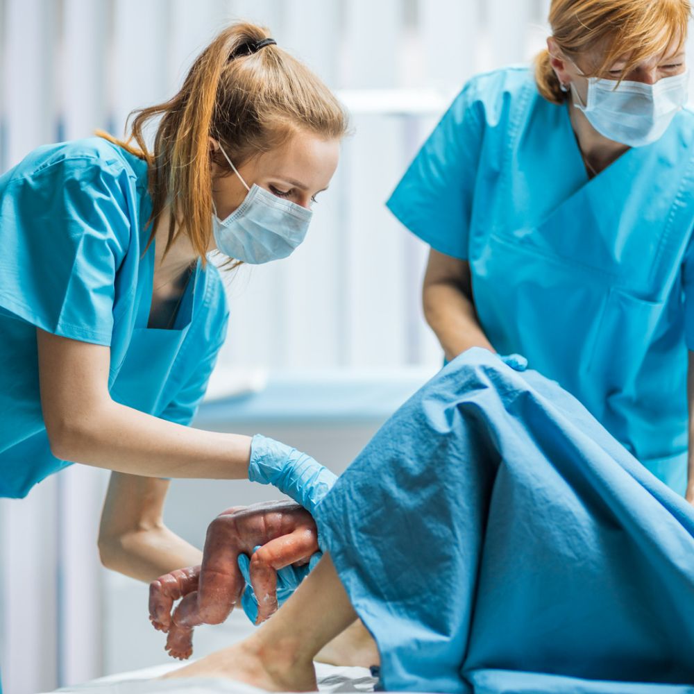 Image of two midwives helping deliver a baby to illustrate the word midwife relating to the spelling of women.